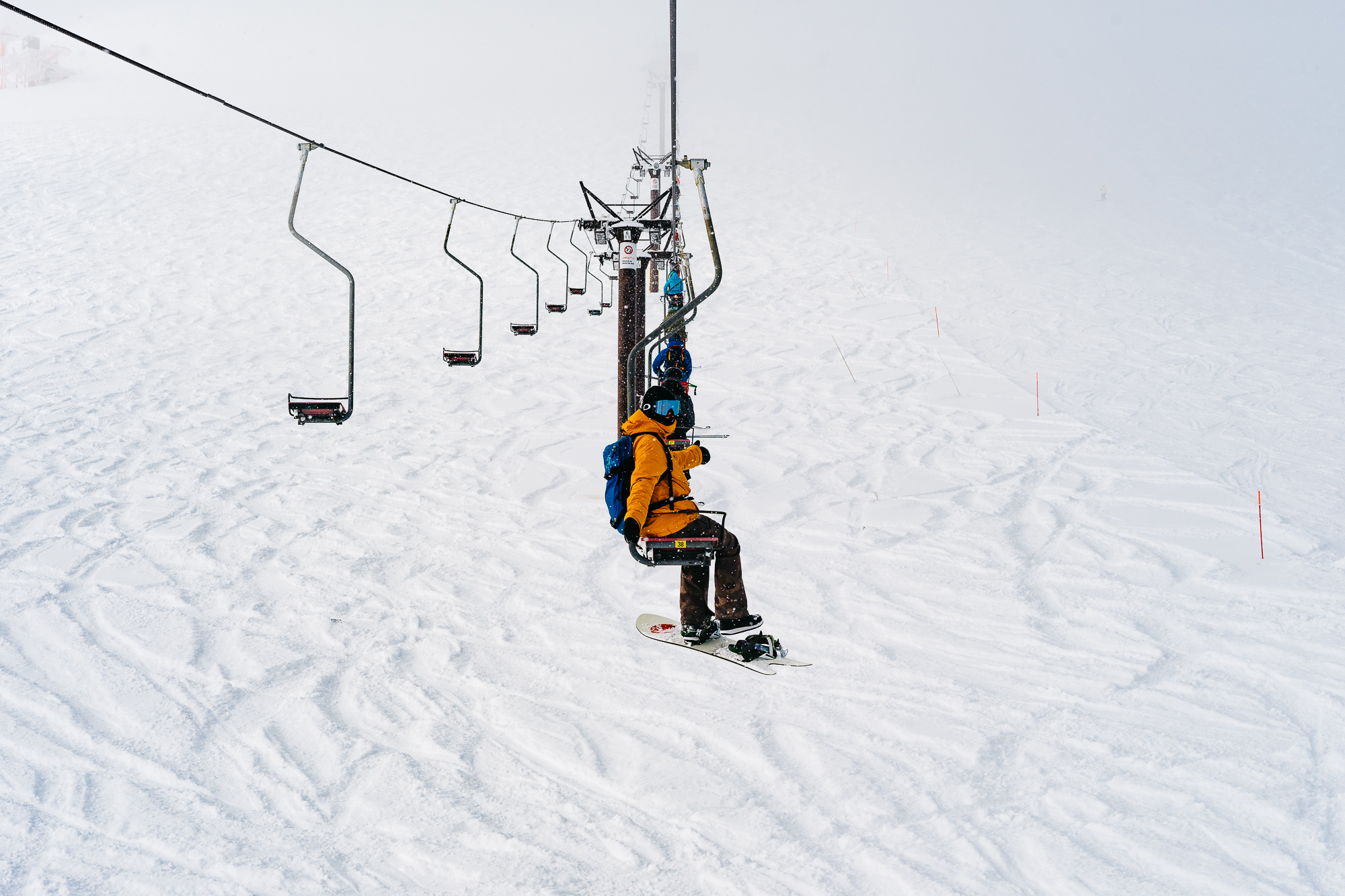 Snowboarder in an yellow jacket on a single-person chairlift over a snowy mountain.