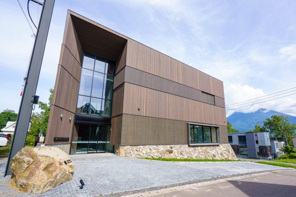 Modern exterior of the newly rebuilt Yukoro Onsen in Hirafu, Niseko, featuring minimalist wood and stone architecture with Mount Yotei visible in the background.