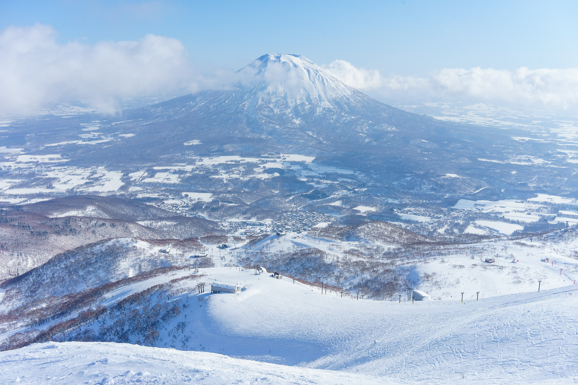 A clear view of the slopes of Niseko ski resort on a sunny day, taken from the summit, with Mount Yotei in the background