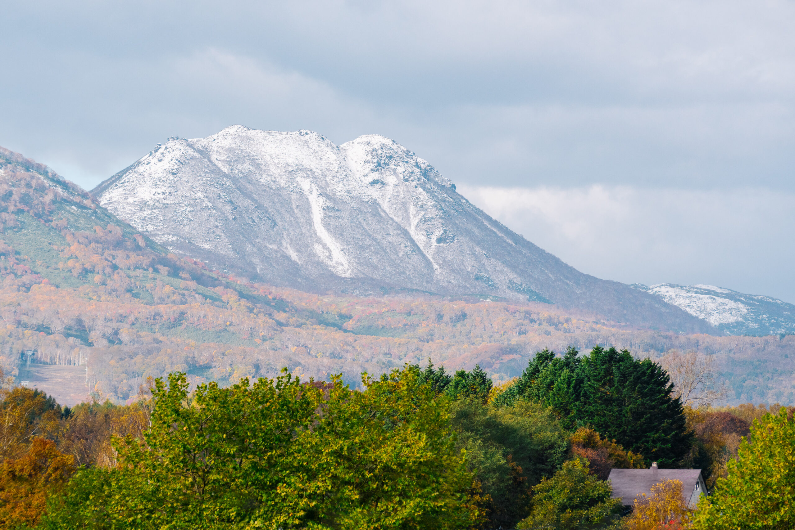 Snow-capped mountain with autumn foliage and colorful trees in the foreground, showing the transition from autumn to winter.