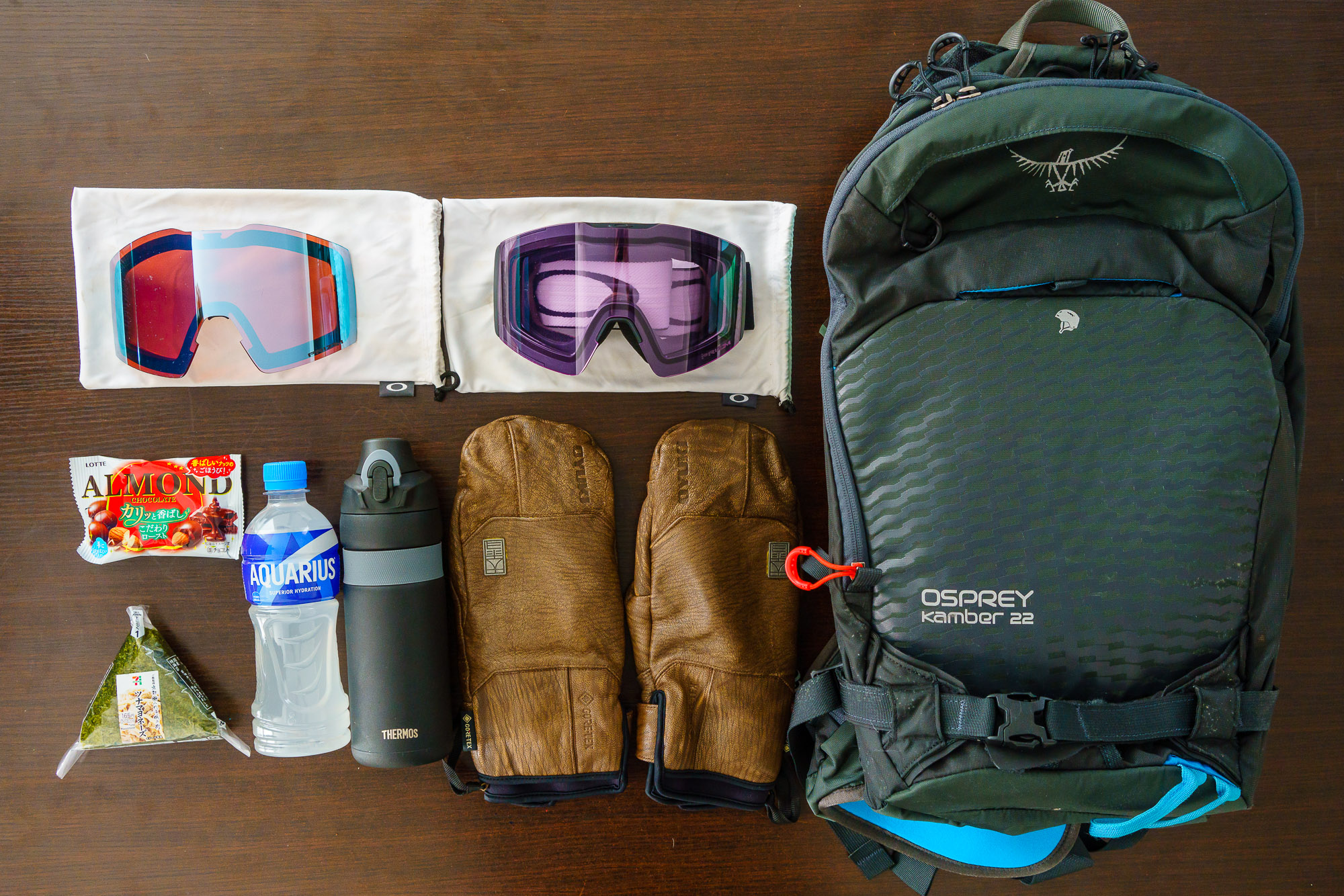 japan-ski-trip-checklist-001 A collection of ski or snowboard gear, including an Osprey Kamber 22 backpack, goggles, mittens, and snacks.