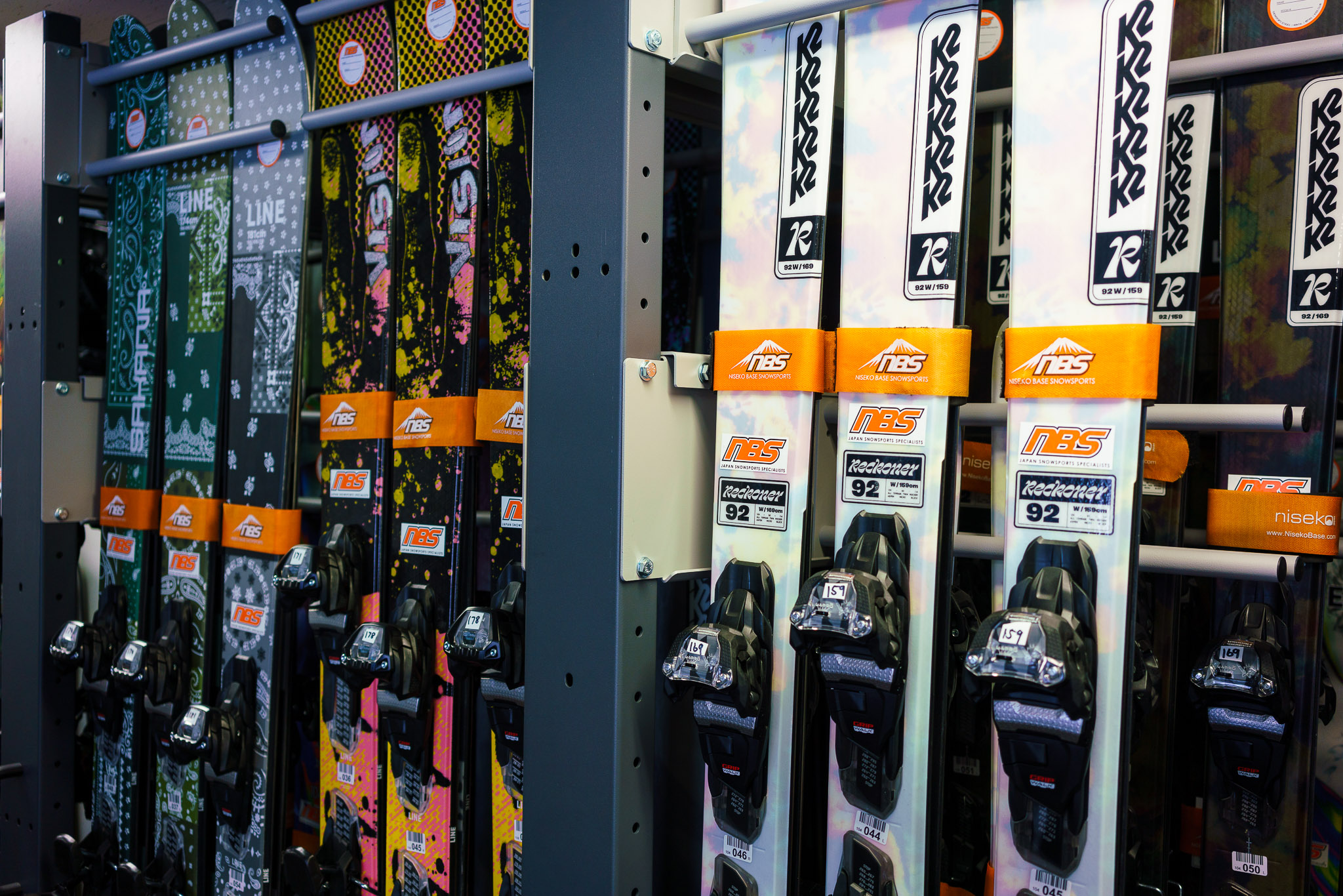 Skiers ride a snowy mountain chairlift above wide powder fields with distant hills and winter landscape in soft, cloudy light.