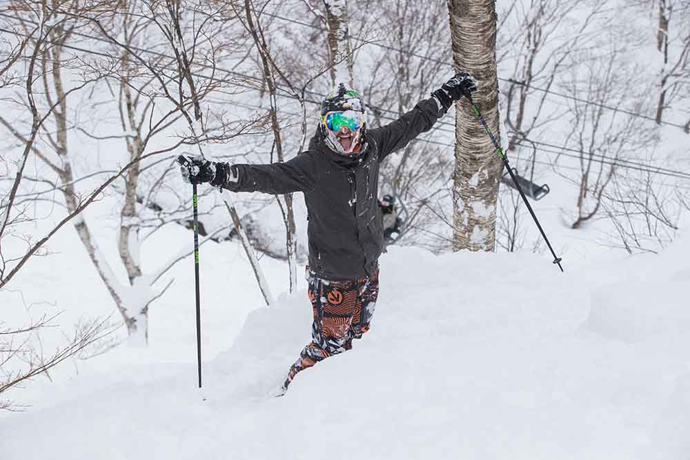 A skier celebrates waist-deep powder among birch trees in Hakuba, Japan and showcasing where to ski in Hakuba and experience epic snow conditions.