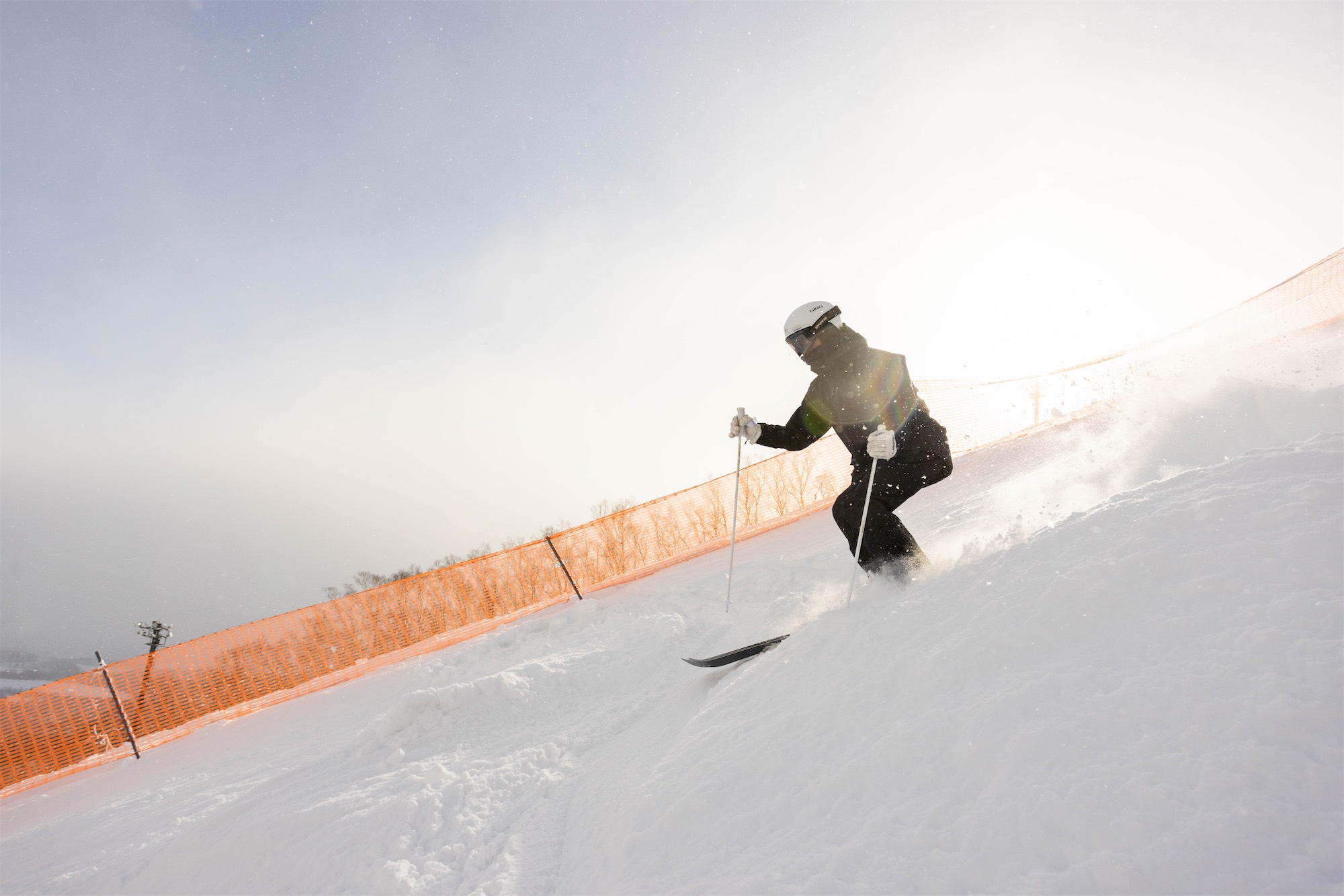 ikuma-horishima-2 Mogul skier Ikuma Horishima doing an aerial trick over a snowy slope with mountain and ski resort in the background.