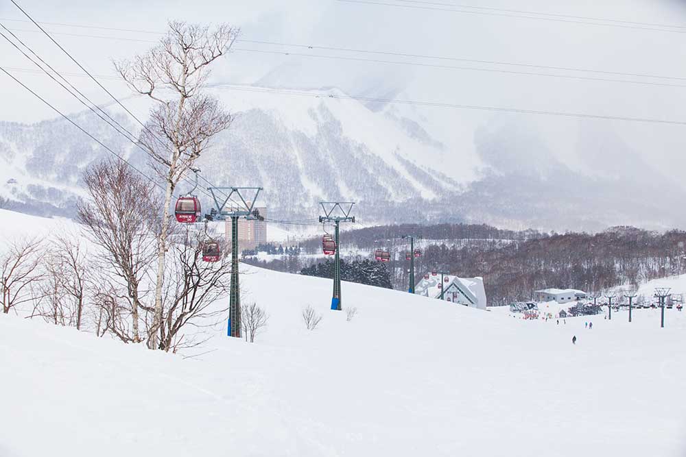 japans-best-ski-resorts-2 Red gondola lifts over snow-covered slopes with mountain backdrop of Rusutsu - also rated as one of the best ski resorts in Japan.