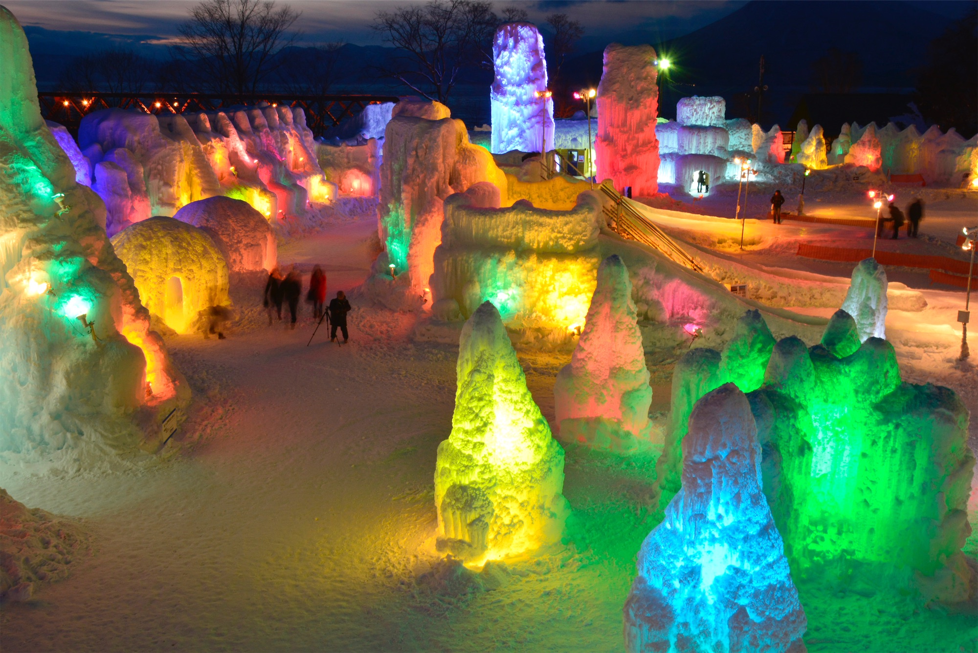 Vibrant lights illuminate towering ice sculptures and igloos in vivid colours at night, creating a magical frozen landscape at the Lake Shikotsu Ice Festival.