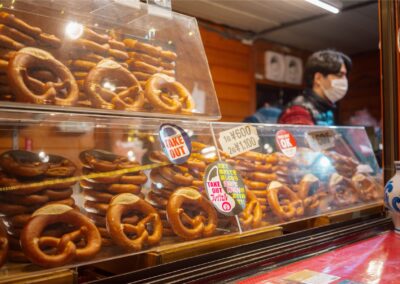 A stall filled with stacks of fresh-looking, golden-brown pretzels for sale at a market, with a vendor nearby.
