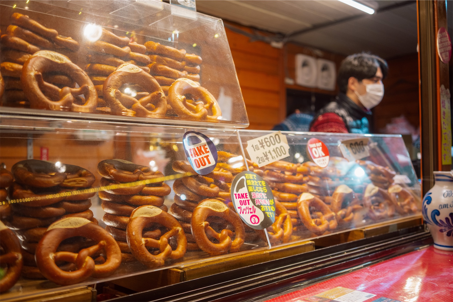 sapporo-christmas-market-2025-10 A stall filled with stacks of fresh-looking, golden-brown pretzels for sale at a market, with a vendor nearby.
