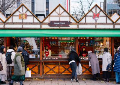 Outdoor market stall named 'SNOWDOME' with multiple people shopping and browsing festive decorations.