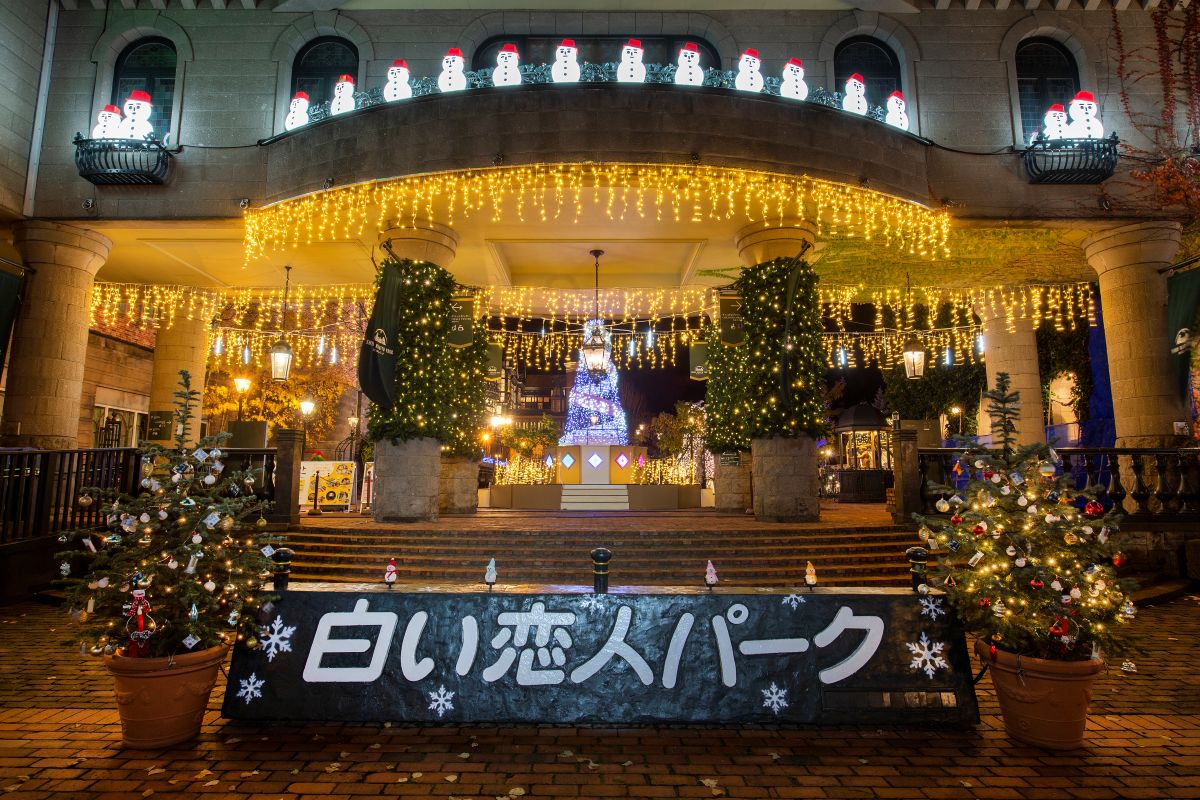 The Shiroi Koibito Park in Sapporo glows with golden fairy lights, Christmas trees, and snowman decorations, creating a festive winter wonderland atmosphere.