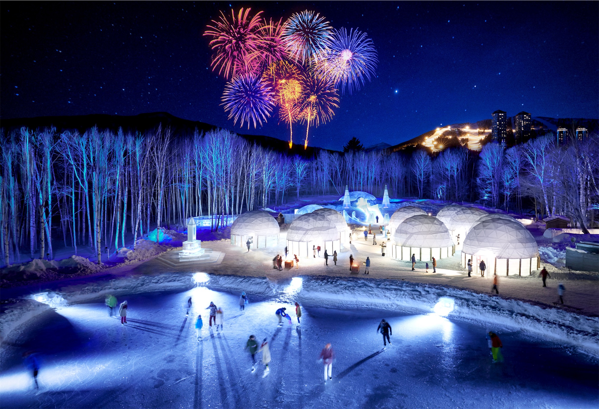 People skate on an illuminated ice rink surrounded by glowing igloos and snow sculptures, as colourful fireworks light up the night sky at Tomamu Ice Village.