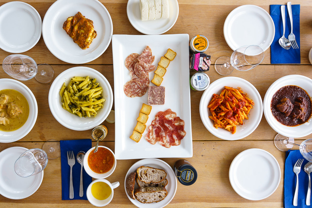 Skiers ride a snowy mountain chairlift above wide powder fields with distant hills and winter landscape in soft, cloudy light.