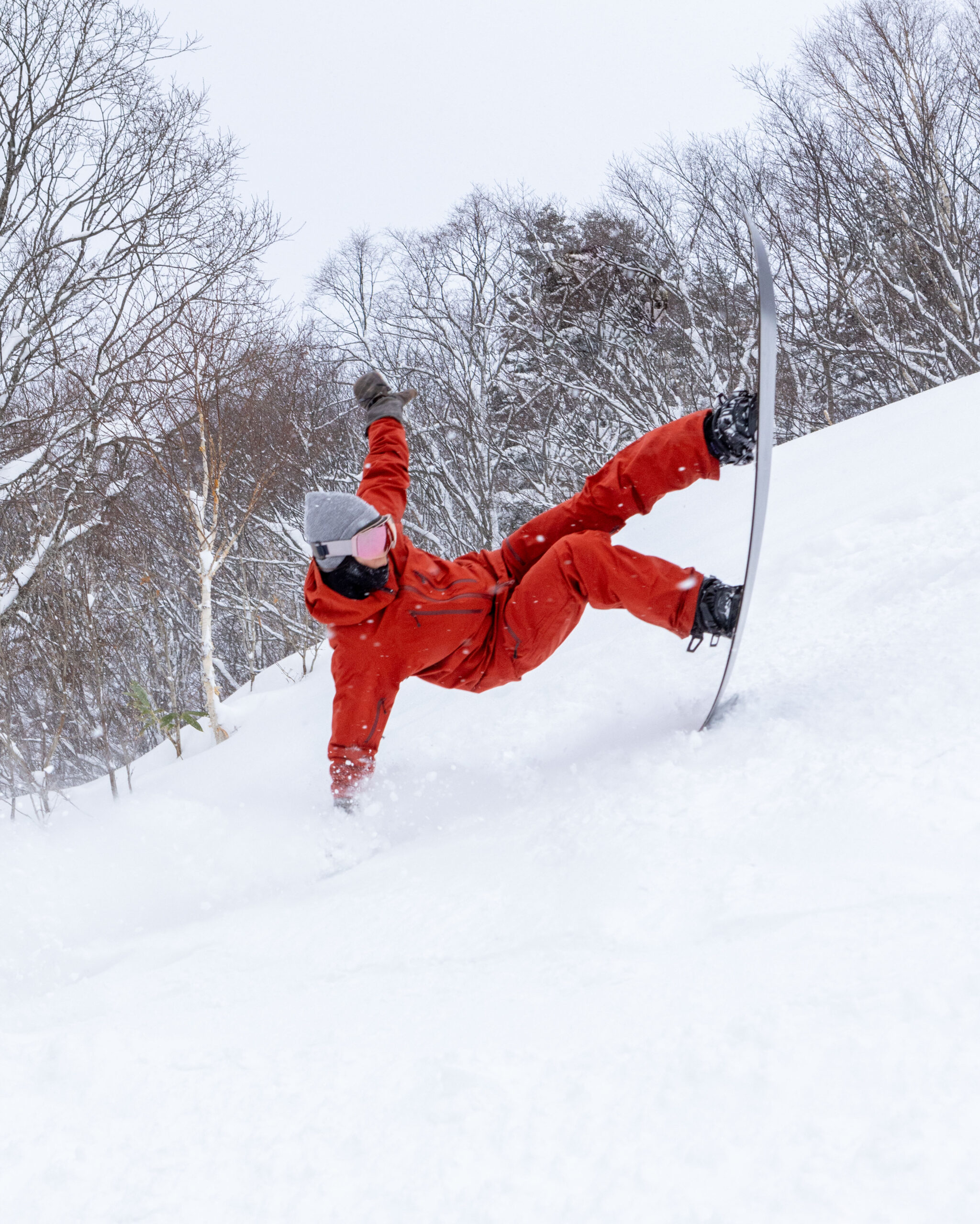 Furano_121423-11 Skier in bright orange jacket carving through deep powder snow among frosty birch trees on a sunny winter day.